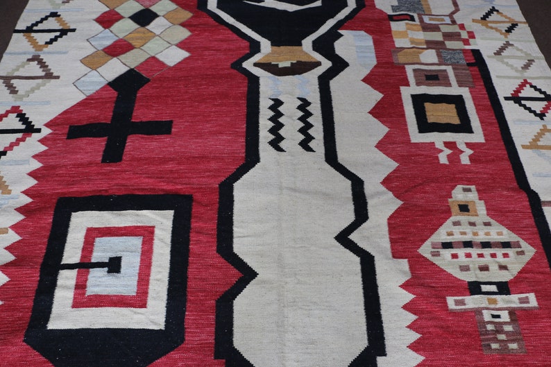 Puede incluir: Una alfombra roja, blanca y negra con un patr&oacute;n geom&eacute;trico de dise&ntilde;o tradicional. La alfombra tiene una variedad de formas y patrones, incluyendo cuadrados, diamantes y zigzags.