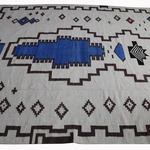 May include: A white rug with a geometric pattern in shades of blue, brown, and black. The rug has a central design that resembles a stylized fish or bird.