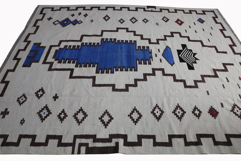 May include: A white rug with a geometric pattern in shades of blue, brown, and black. The rug has a central design that resembles a stylized fish or bird.