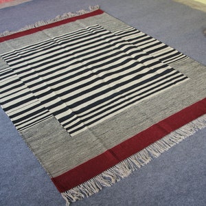 May include: A black and white striped rug with a red border and fringe. The rug is made of woven fabric and has a geometric pattern.