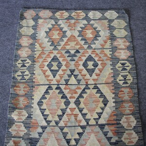 May include: A traditional rug with a geometric pattern in shades of blue, red, and white. The rug has a woven texture and a fringed edge.