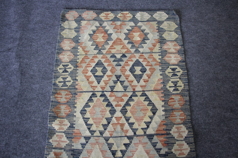 May include: A traditional rug with a geometric pattern in shades of blue, red, and white. The rug has a woven texture and a fringed edge.
