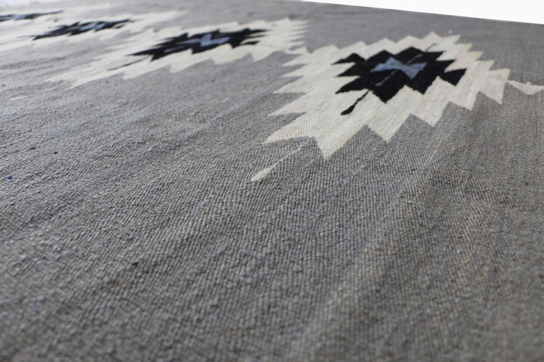 May include: A grey woven rug with a white and black geometric pattern. The rug has a textured surface.