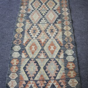 May include: A long, narrow rug with a geometric pattern in shades of blue, red, and cream. The rug has a traditional, hand-woven look.