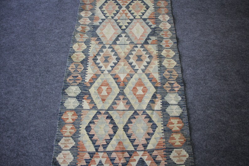 May include: A long, narrow rug with a geometric pattern in shades of blue, red, and cream. The rug has a traditional, hand-woven look.