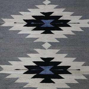 May include: A grey and white woven rug with a geometric pattern in black and blue. The pattern is repeated twice on the rug.