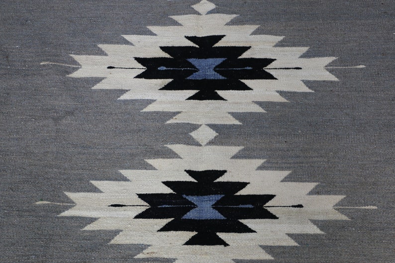 May include: A grey and white woven rug with a geometric pattern in black and blue. The pattern is repeated twice on the rug.