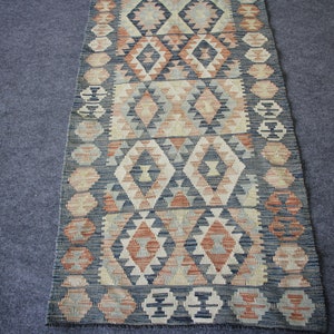 May include: A long, narrow rug with a geometric pattern in shades of blue, beige, and red. The rug has a traditional, woven look.