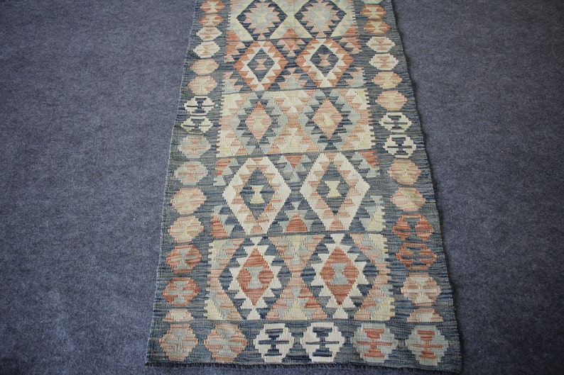 May include: A long, narrow rug with a geometric pattern in shades of blue, beige, and red. The rug has a traditional, woven look.