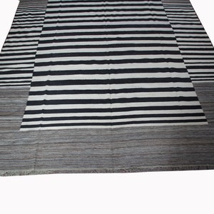 May include: Black and white striped rug with a gray border. The rug has a contemporary design and is made of wool.