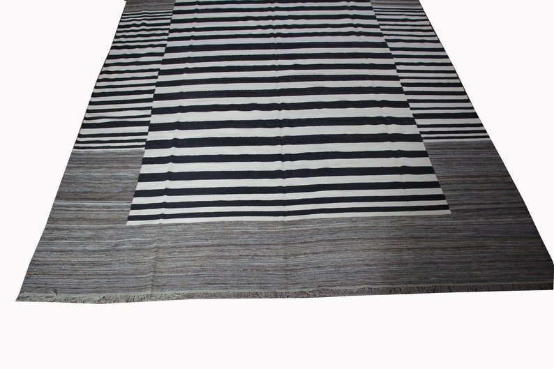 May include: Black and white striped rug with a gray border. The rug has a contemporary design and is made of wool.