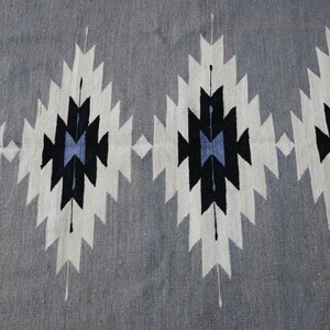 May include: A grey rug with a geometric pattern in black, white, and blue. The pattern is made up of repeating diamonds and triangles.