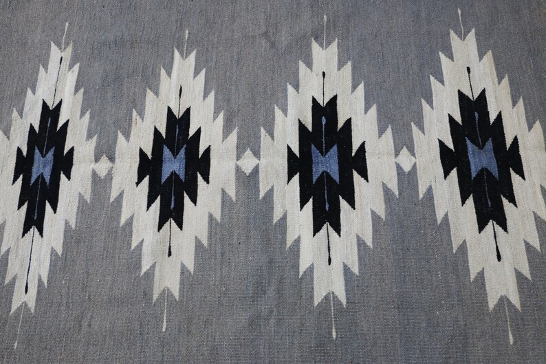May include: A grey rug with a geometric pattern in black, white, and blue. The pattern is made up of repeating diamonds and triangles.