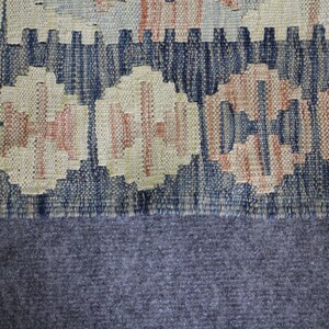May include: Close-up of a woven rug with a blue, beige and orange geometric pattern. The rug has a fringe border and is made of a soft, textured material.