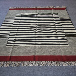 May include: A black and white striped rug with a red border and fringe. The rug has a geometric pattern with a central square.