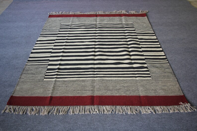 May include: A black and white striped rug with a red border and fringe. The rug has a geometric pattern with a central square.