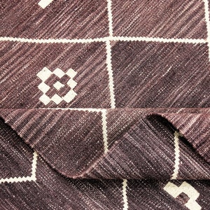 May include: A close-up of a brown and white woven rug with a geometric pattern. The rug is folded in half, showing the texture of the fabric.