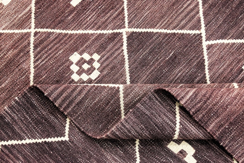 May include: A close-up of a brown and white woven rug with a geometric pattern. The rug is folded in half, showing the texture of the fabric.