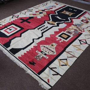 Puede incluir: Una alfombra blanca, roja, negra y beige con un patr&oacute;n geom&eacute;trico. La alfombra tiene un borde de flecos.