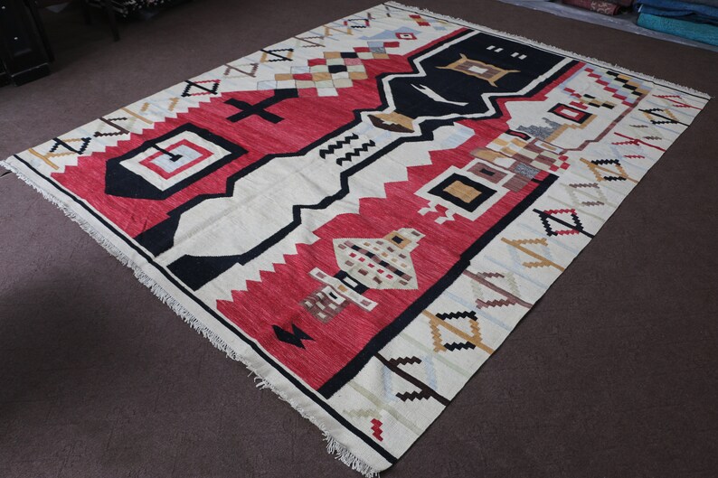 Puede incluir: Una alfombra blanca, roja, negra y beige con un patr&oacute;n geom&eacute;trico. La alfombra tiene un borde de flecos.