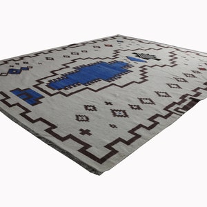May include: A white rug with a geometric pattern in brown and blue. The rug has a fringe border.