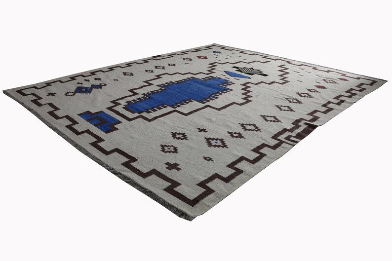 May include: A white rug with a geometric pattern in brown and blue. The rug has a fringe border.