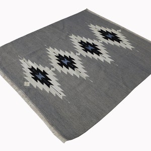 May include: A grey rug with a white and black geometric pattern. The pattern features a series of diamond shapes with a blue centre.