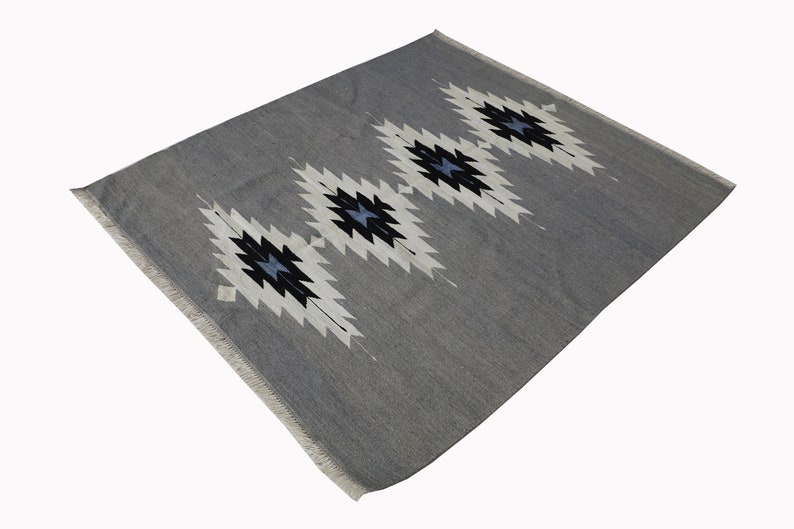 May include: A grey rug with a white and black geometric pattern. The pattern features a series of diamond shapes with a blue centre.