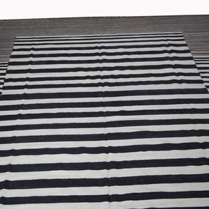 May include: Black and white striped rug with a gray border. The rug has a woven texture.