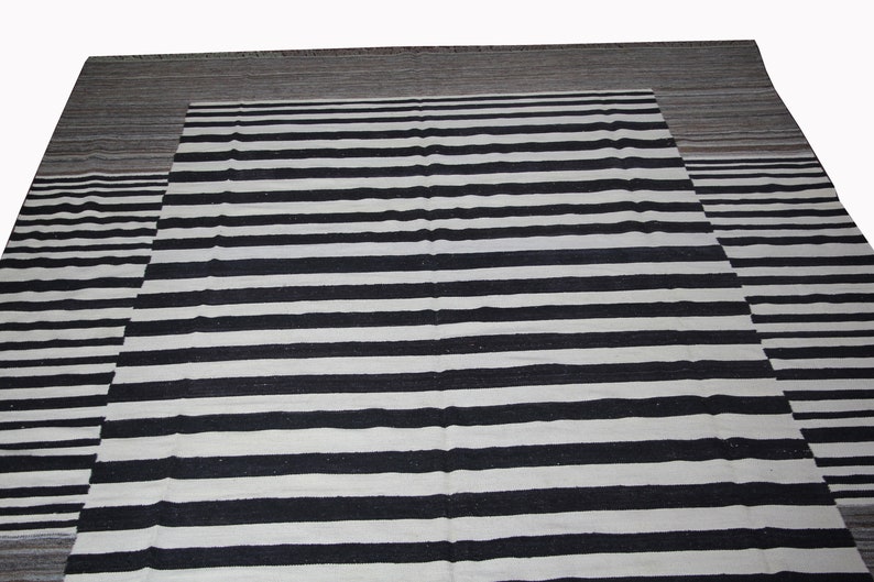 May include: Black and white striped rug with a gray border. The rug has a woven texture.