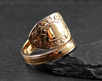 May include: A gold ring with an intricate design. The ring is made of two bands, one of which is wider and has a raised, oval-shaped design.