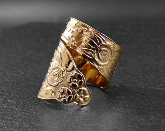 May include: A gold ring with a floral design. The ring is made of metal and has a textured surface.