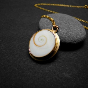 Peut inclure: Un collier en chaîne dorée avec un pendentif en forme de coquille blanche avec un motif en spirale.