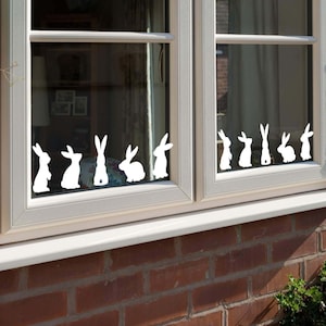 May include: A window with a row of white bunny silhouettes on the glass. The bunnies are facing the viewer and are arranged in a line across the window.