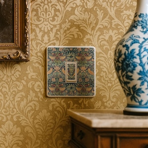 May include: A square light switch cover plate featuring a detailed botanical pattern with birds, flowers, and foliage in shades of green, orange, and brown. The central toggle switch is also covered in the same matching intricate floral print.