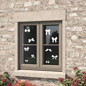 Peut inclure: Une fenêtre avec des autocollants en forme de nœud blanc sur le verre. La fenêtre est encadrée de bois brun et est encastrée dans un mur en pierre.