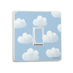 Puede incluir: Una tapa de interruptor de luz azul claro con un borde blanco y un interruptor de luz blanco. La tapa tiene un patrón de nubes blancas sobre un fondo azul claro. El texto "stika.co" está impreso en la esquina inferior derecha.
