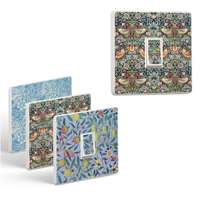 Puede incluir: Tres tapas de interruptor de luz con diferentes patrones florales. La primera tapa tiene un patrón floral azul y blanco, la segunda tapa tiene un patrón floral azul, verde y rojo, y la tercera tapa tiene un patrón floral azul y verde con fruta.