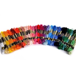 May include: A collection of embroidery floss spools in a rainbow of colors, arranged in a semi-circle. The spools are all the same size and have black labels with gold lettering.