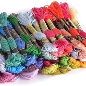 May include: A collection of embroidery floss spools in a variety of colors, including pink, blue, green, yellow, orange, and red. The spools are arranged in a pile, with the ends of the floss visible.