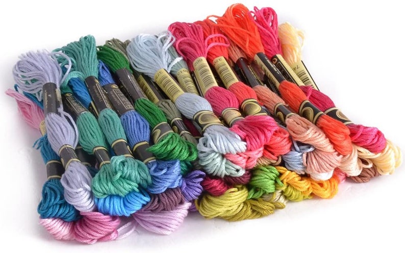 May include: A collection of embroidery floss spools in a variety of colors, including pink, blue, green, yellow, orange, and red. The spools are arranged in a pile, with the ends of the floss visible.
