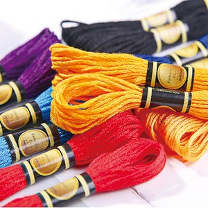May include: Assortment of embroidery floss spools in various colors, including purple, yellow, blue, red, and black. Each spool has a gold label with the text "COLORCHART" and "Embroidery Cotton" printed on it.