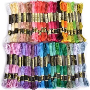May include: A collection of 50 embroidery floss spools in a variety of colors, including pink, purple, blue, green, yellow, orange, red, and brown. Each spool is labeled with the brand name "Anchor" and a number.