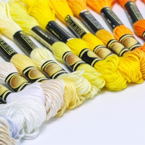 May include: A collection of embroidery floss spools in various shades of white, yellow, and orange. The spools are arranged in a gradient from white to orange.