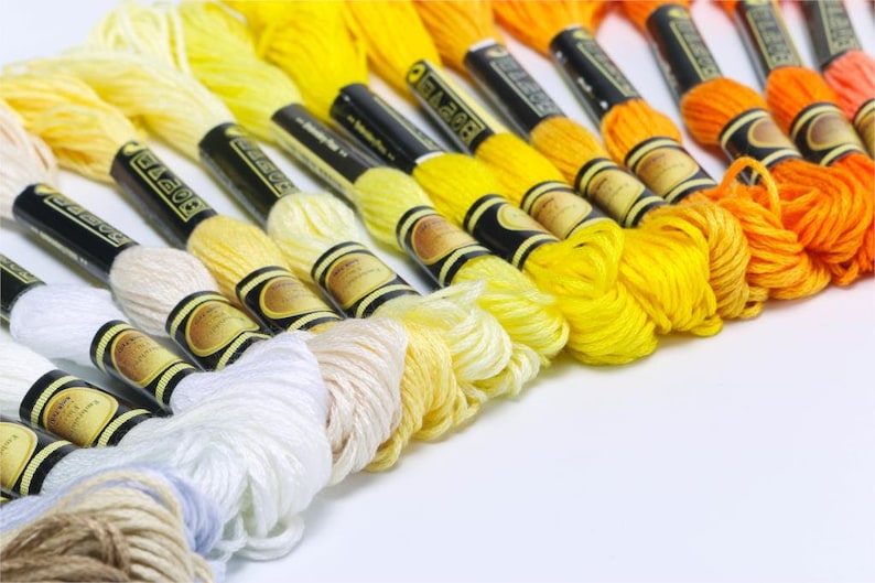 May include: A collection of embroidery floss spools in various shades of white, yellow, and orange. The spools are arranged in a gradient from white to orange.