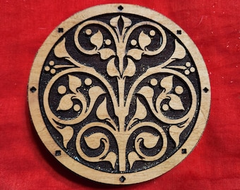 Puede incluir: Un posavasos redondo de madera con un intrincado diseño floral en negro y marrón. El diseño presenta un tallo central con hojas y espirales.