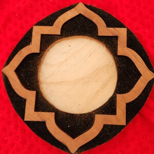 May include: A wooden coaster with a black center and a decorative, carved, light brown design. The coaster has a round, light brown center.