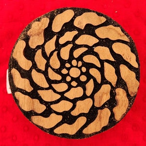 May include: A round wooden block with a black and brown swirl design. The design is carved into the wood and creates a spiral pattern.