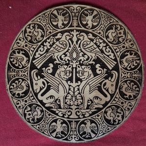 May include: A circular wooden plaque featuring intricate pyrography. The center displays two mirrored winged griffins facing each other, topped by two birds. The outer border is decorated with a repeating pattern of small birds within circular frames.