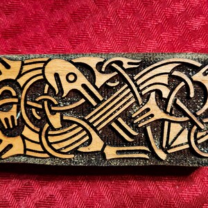 May include: A wooden plaque with a carved Celtic knot design in brown and black. The knotwork is intricate and detailed, with a variety of shapes and patterns.